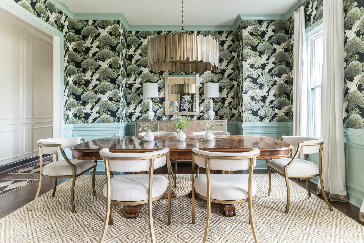 A dining room and entry with a round table, upholstered chairs and layered lighting