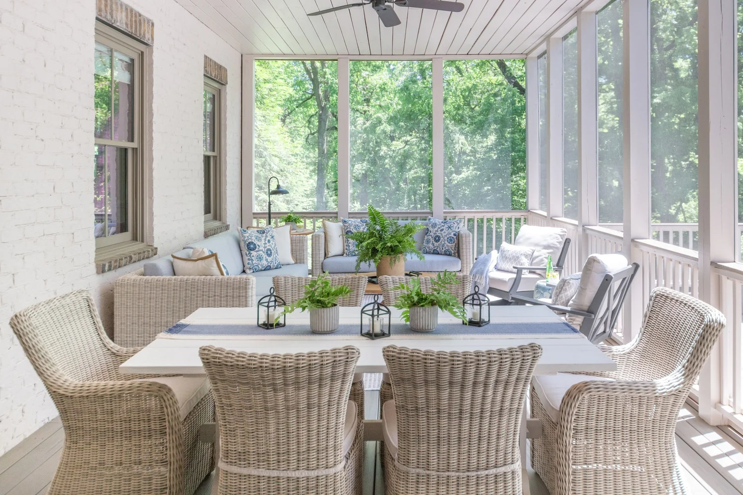 Screened porch with white wicker dining chairs, a painted table and a woven sofa set against painted brick