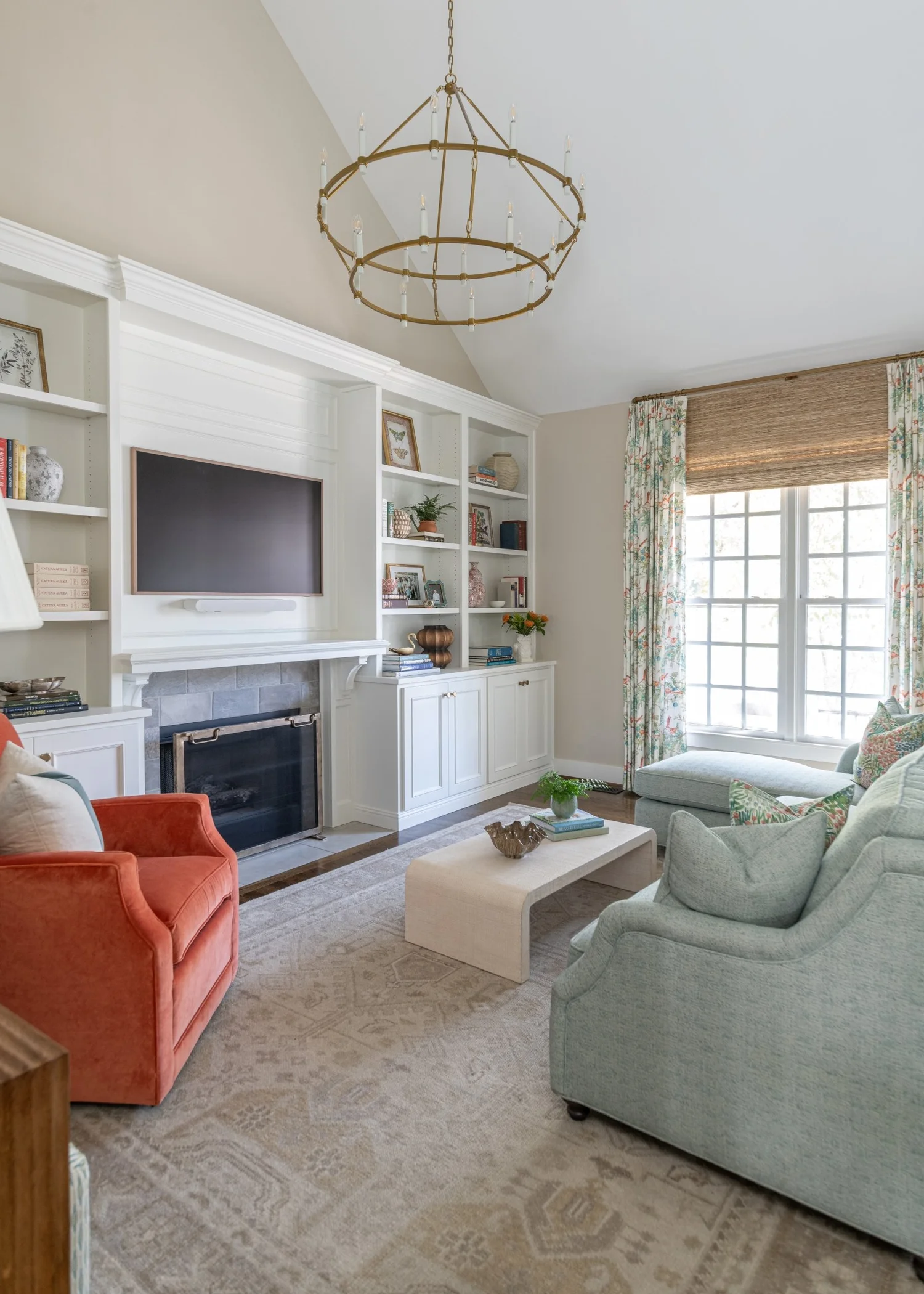 Vaulted living room with white built-ins flanking a fireplace, a coral armchair and a sage sofa on a faded rug