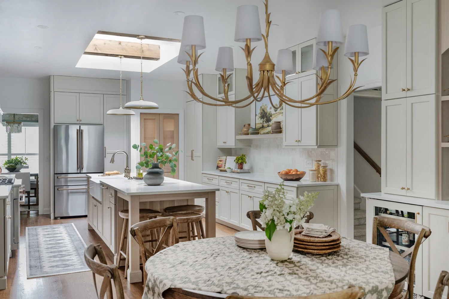 Pale grey-green kitchen with a white island, gold chandelier and a skylight spilling daylight across oak floors