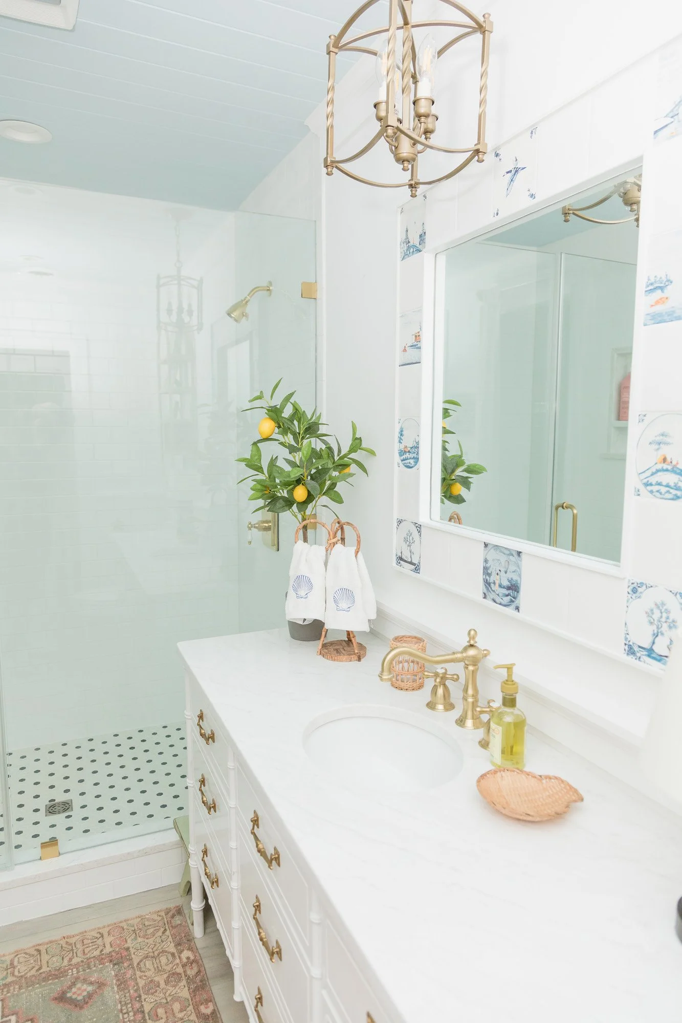 Long white vanity with a marble top and brass faucet, facing a glass shower under a pale blue ceiling
