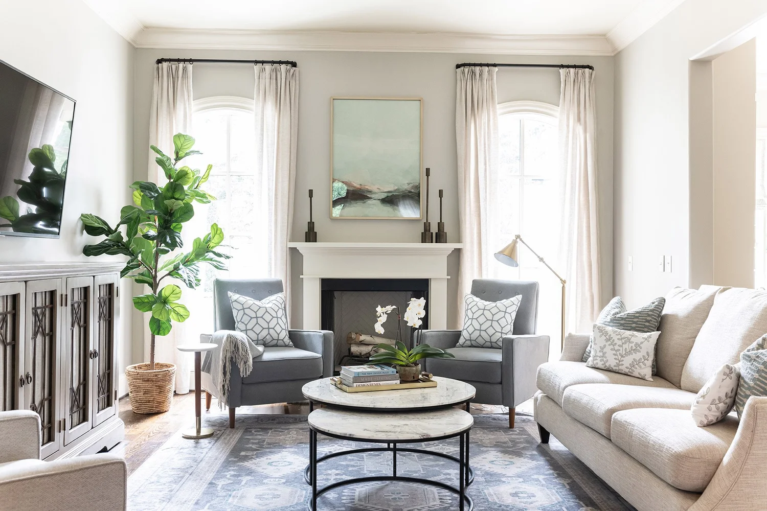 Symmetrical living room with grey chairs at a white fireplace, a cream sofa and arched windows in daylight